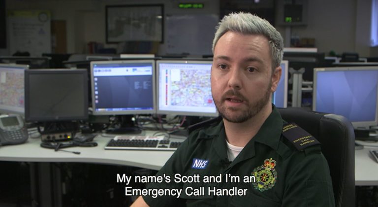 Scott in uniform in front of control room screens