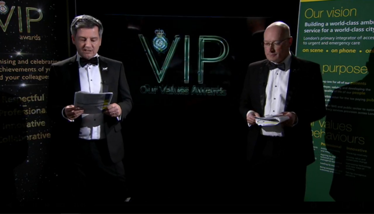 The presenters in suits ahead of a screen which reads VIP Awards