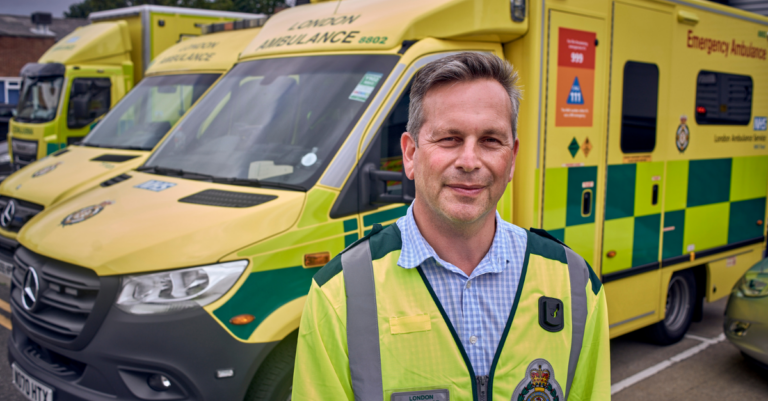 Daniel Elkeles in a LAS top in front of a row of ambulances
