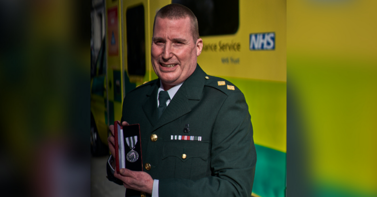 Jason in dress uniform holds his medal photographed in front of an ambulance