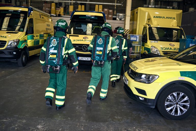 A picture of three HART paramedics in special protective uniforms, with lots of ambulance vehicles visible in the background.