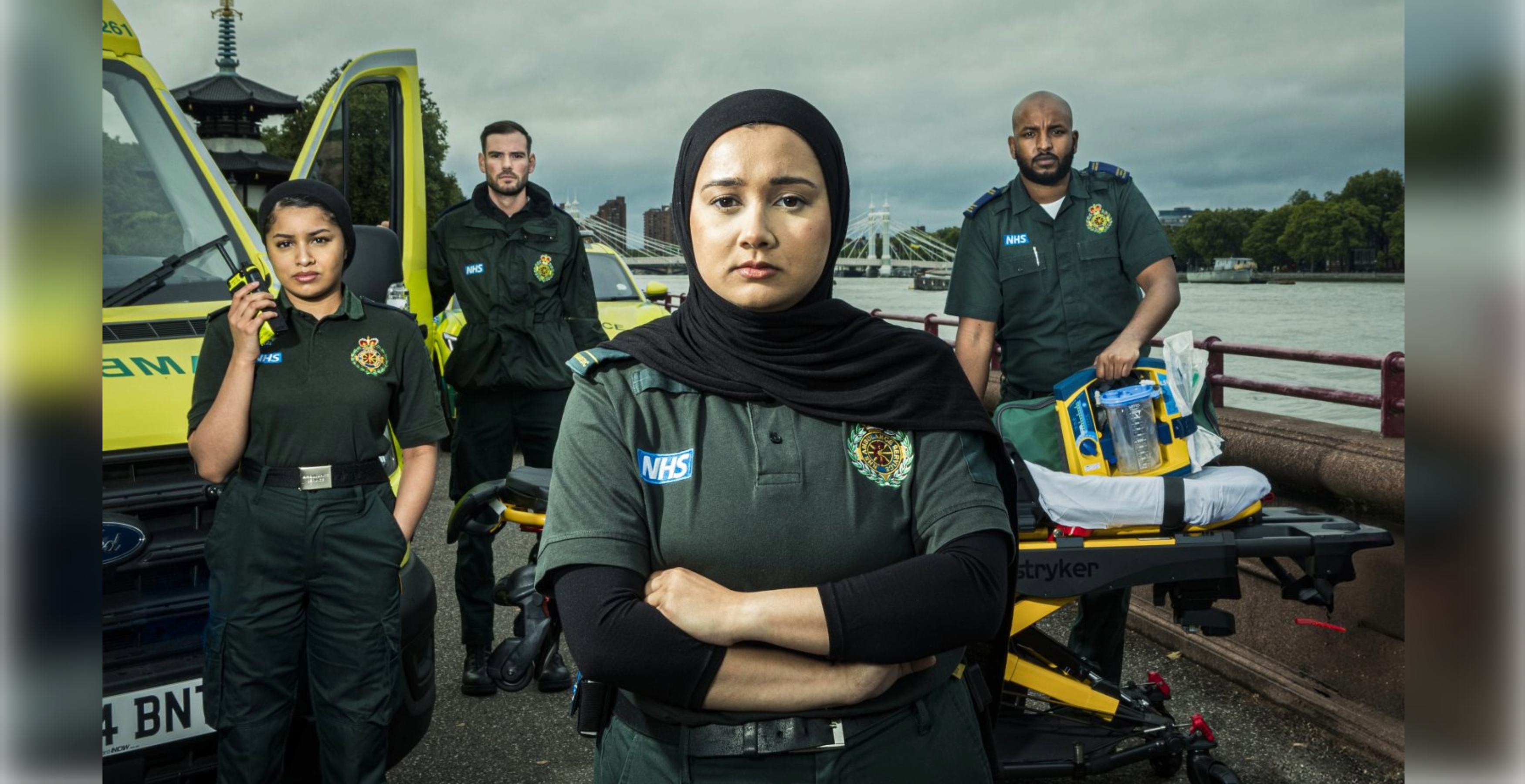 Four ambulance clinicians with an ambulance in the background near the Thames river.