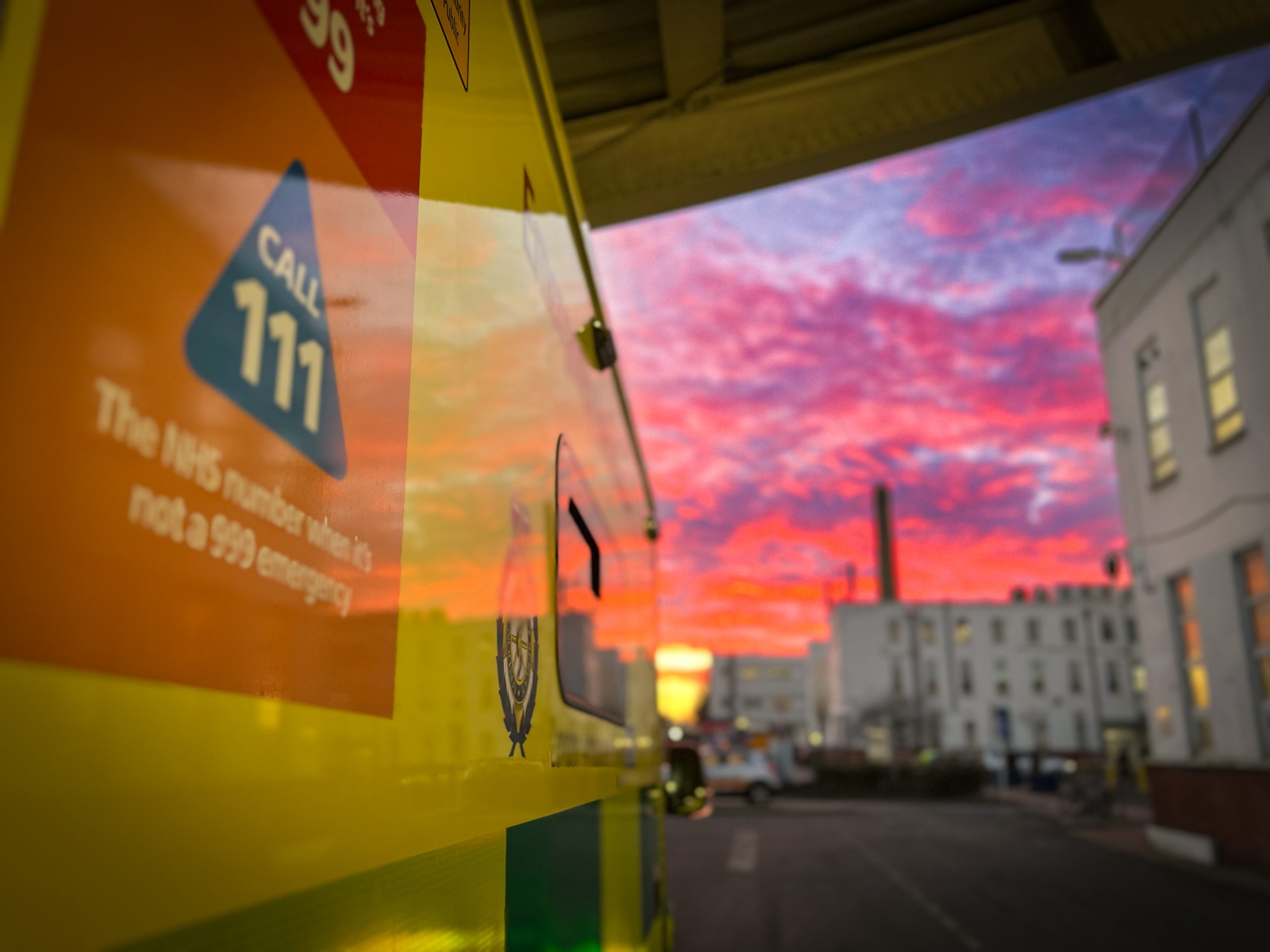 Ambulance at a hospital, with a red and purple sky visible.