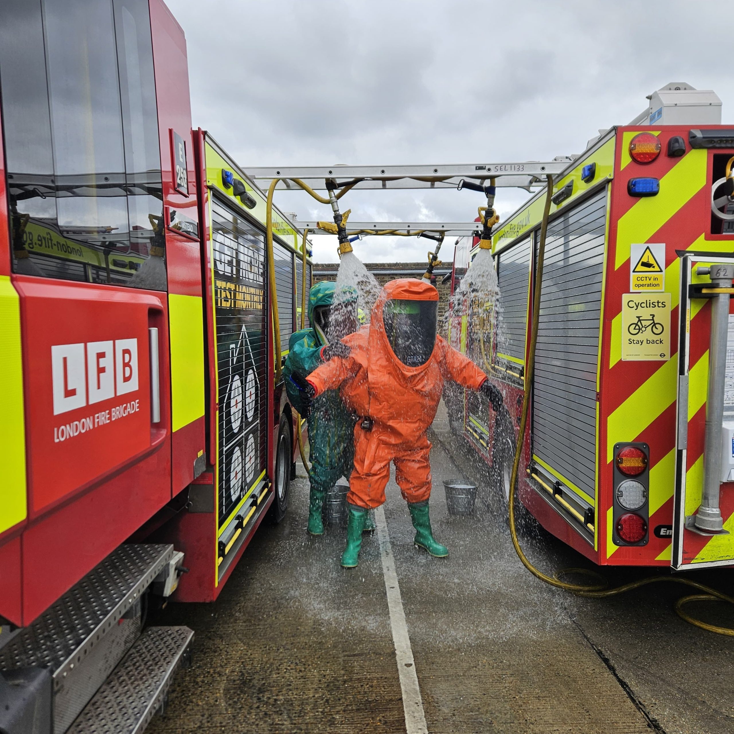 Specialist response staff in HAZMAT suits at a training exercise, with LFB vehicles visible.