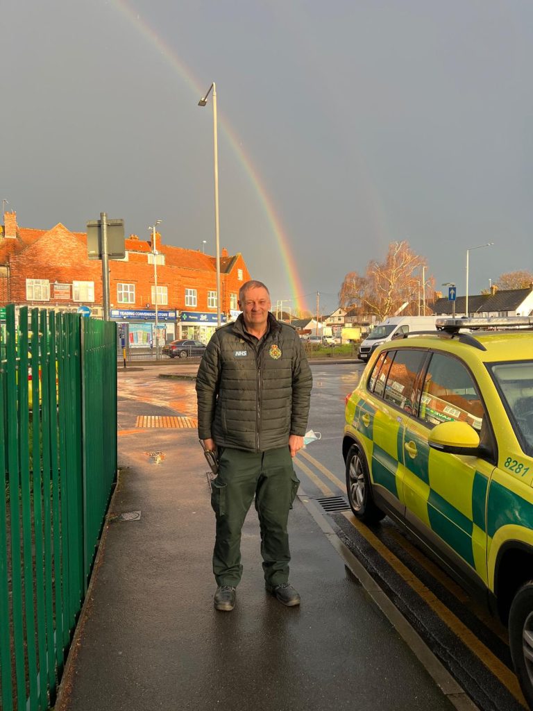 Paramedic next to a FRV with a rainbow behind him