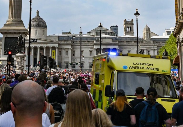 Crowds gathering in Trafalgar Square with an ambulance on standby.