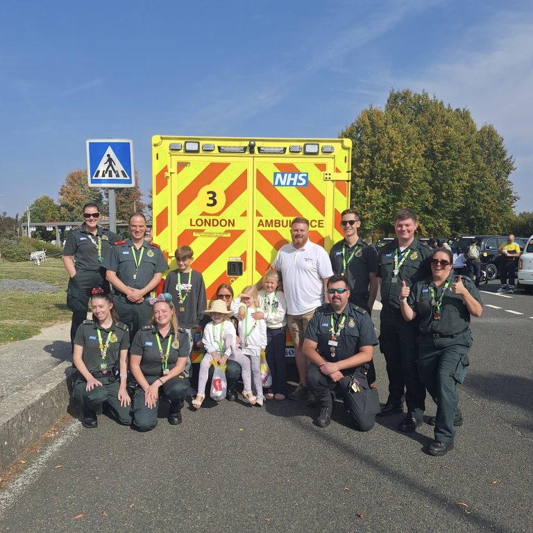 Children and paramedics posing in front of an ambulance wearing micky ears