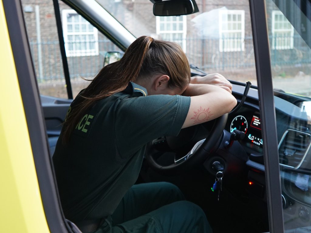 Paramedic with head in hands in driving seat of stationary ambulance.