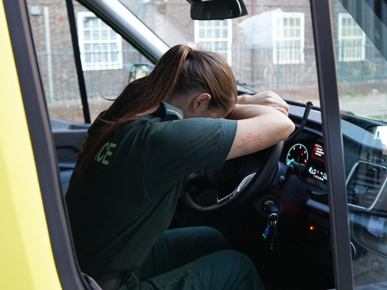 Paramedic with head in hands in driving seat of stationary ambulance.