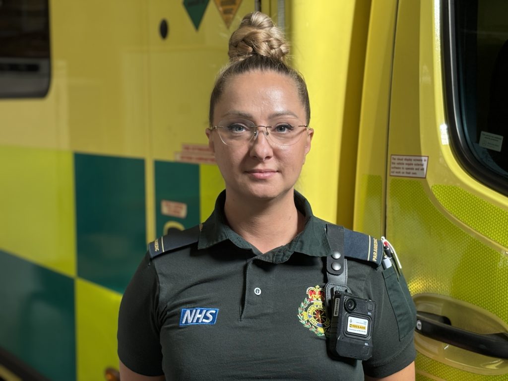 Paramedic Gosha in her ambulance uniform, wearing a body-worn camera.